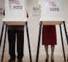 a man and woman standing in a room with voting boxes