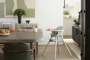  A kitchen decorated in grays and pale greens. In the center of the picture is Lalo's Chair, a convertible three-in-one highchair with four widespread wooden legs. This chair is pastel green and has sliced oranges on its tray. 