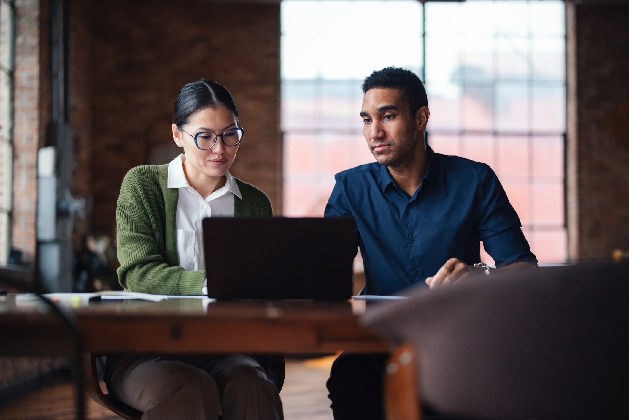 Two office workers are concerned at what they are reading on a laptop.